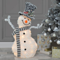 Happy snowman light upChristmas decoration with grey and white scarf, top hat with pine foliage, sitting beside a silver Christmas tree with presents