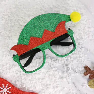 green and red glitter elf hat novetly glasses with yellow pom pom on snow covered background