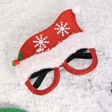 red glitter santa glasses with santa hat design styled on white background with artificial snow