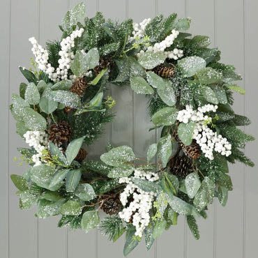 white berry pine cone frosted christmas wreath hanging on grey door