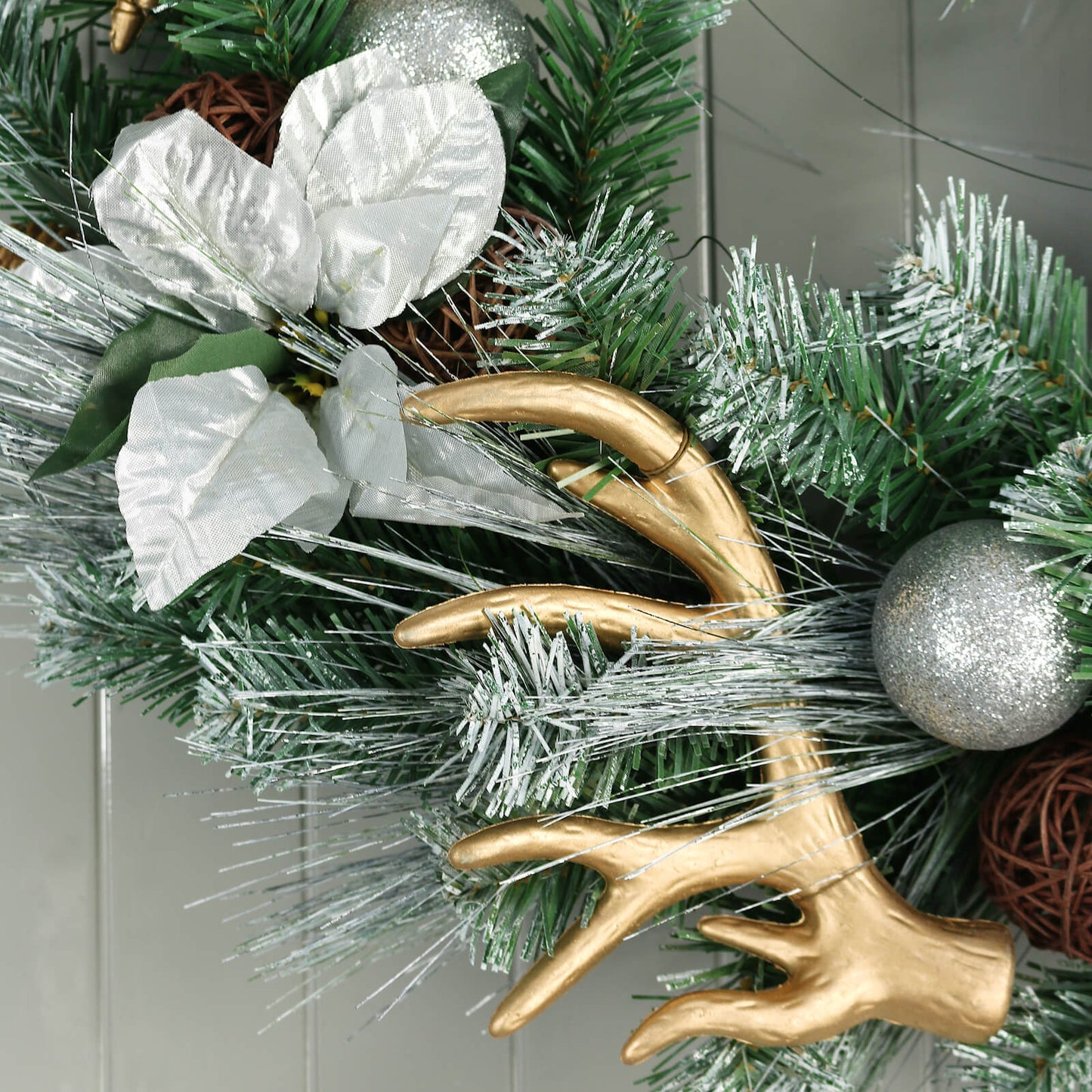 artifical gold coloured antler with silver leaves and silver glitted christmas bauble on snowy wreath foliage