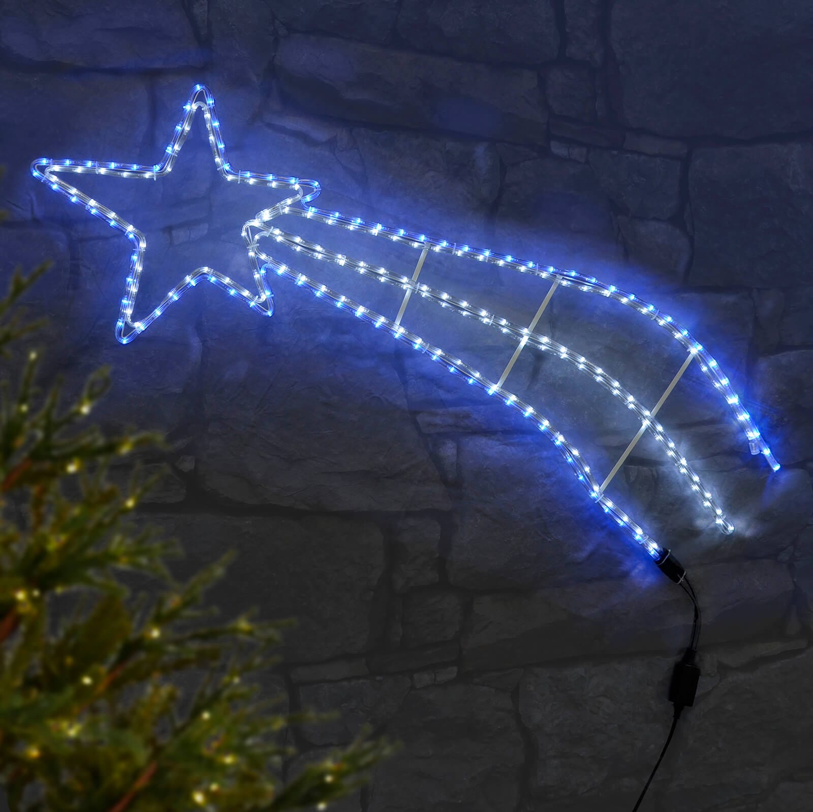 Blue and white shooting star rope light Christmas garden decoration on a stone wall with Christmas tree