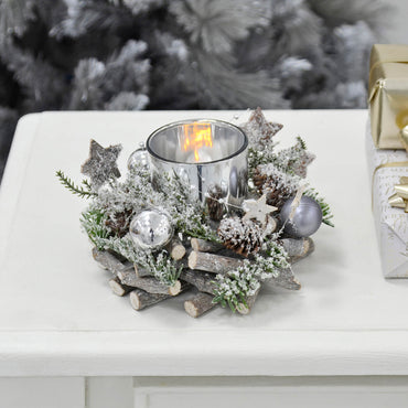 Mr Crimbo silver Christmas candle holder with round grey twig base, silver baubles, stars, pine cones and foliage on a white table with Christmas presents