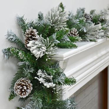 Christmas garland with snow flocked green pine branches and pine cones on a white mantelpiece