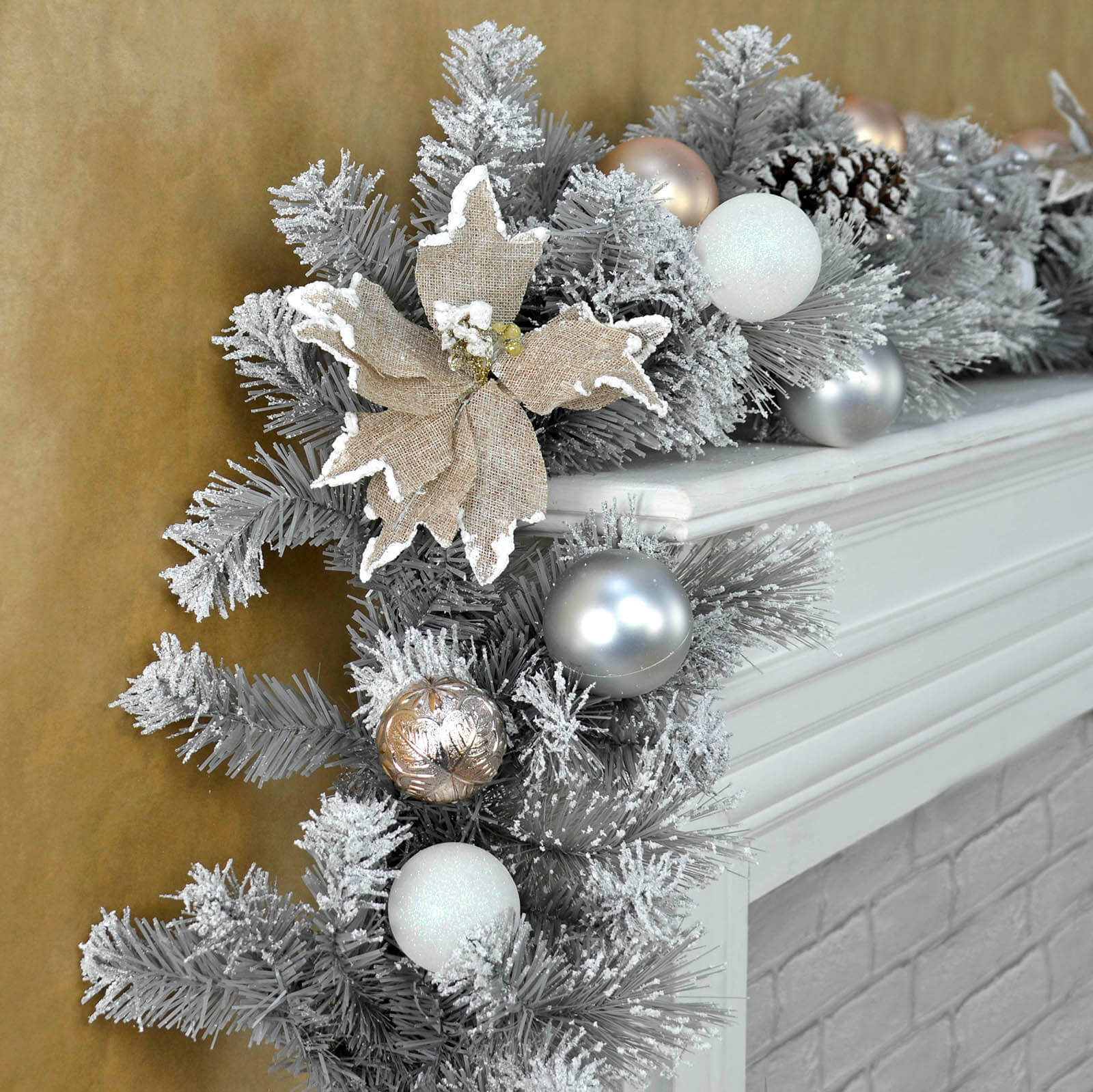 snowy grey garland on fireplace ledge featuring hessian poinsettia, silver gold and white baubles and glittery tips