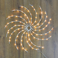 Light up swirl wheel Christmas wall decoration with warm white LED lights, hanging on a wood panelled wall
