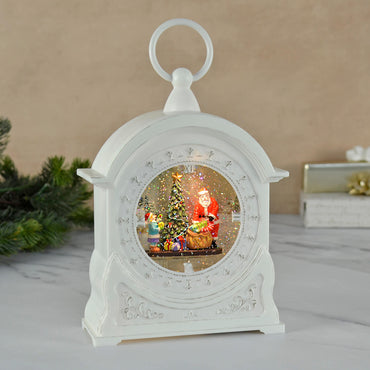 Carriage clock shape Christmas decoration with glitter water snow scene on a grey marble table with foliage and presents