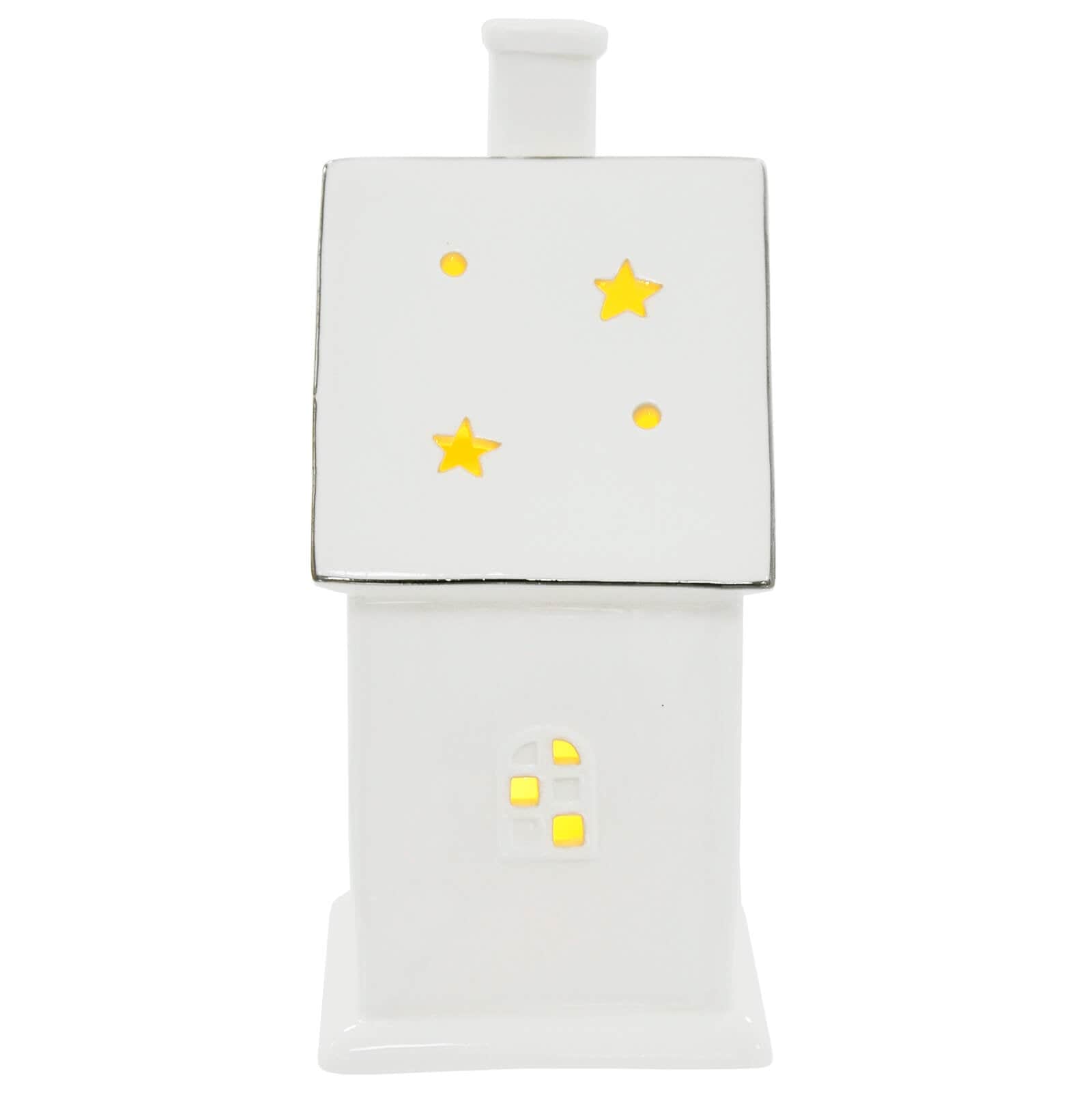 Side view of white ceramic house Christmas ornament with warm white LED light shining through a window and cut away stars