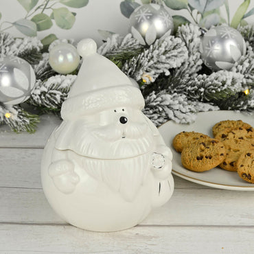 Santa Christmas storage jar in white with silver detail on a wooden table with plate of chocolate chip cookies, Christmas garland and silver baubles