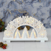 white wooden Christmas arch light up decoration with snowflakes, stars and trees on a white tile tabletop with pine cones and marble wallpaper