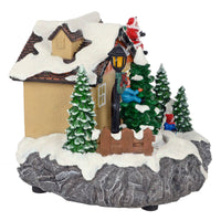 Side view of Christmas snow scene ornament with house, trees, Santa on the roof and children playing
