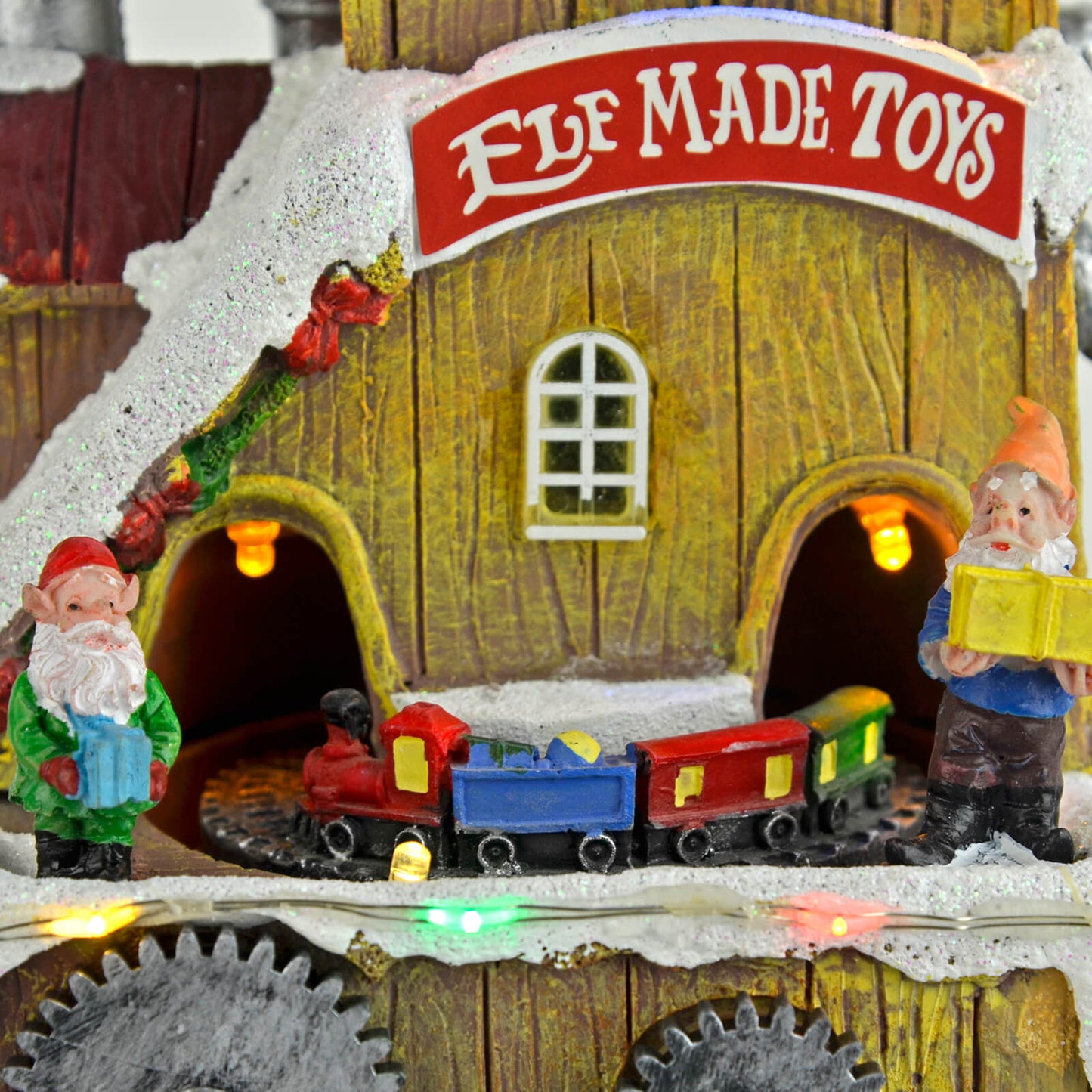 Close up of 2 elves at Elf Made Toys with presents beside a train lit by LED lights