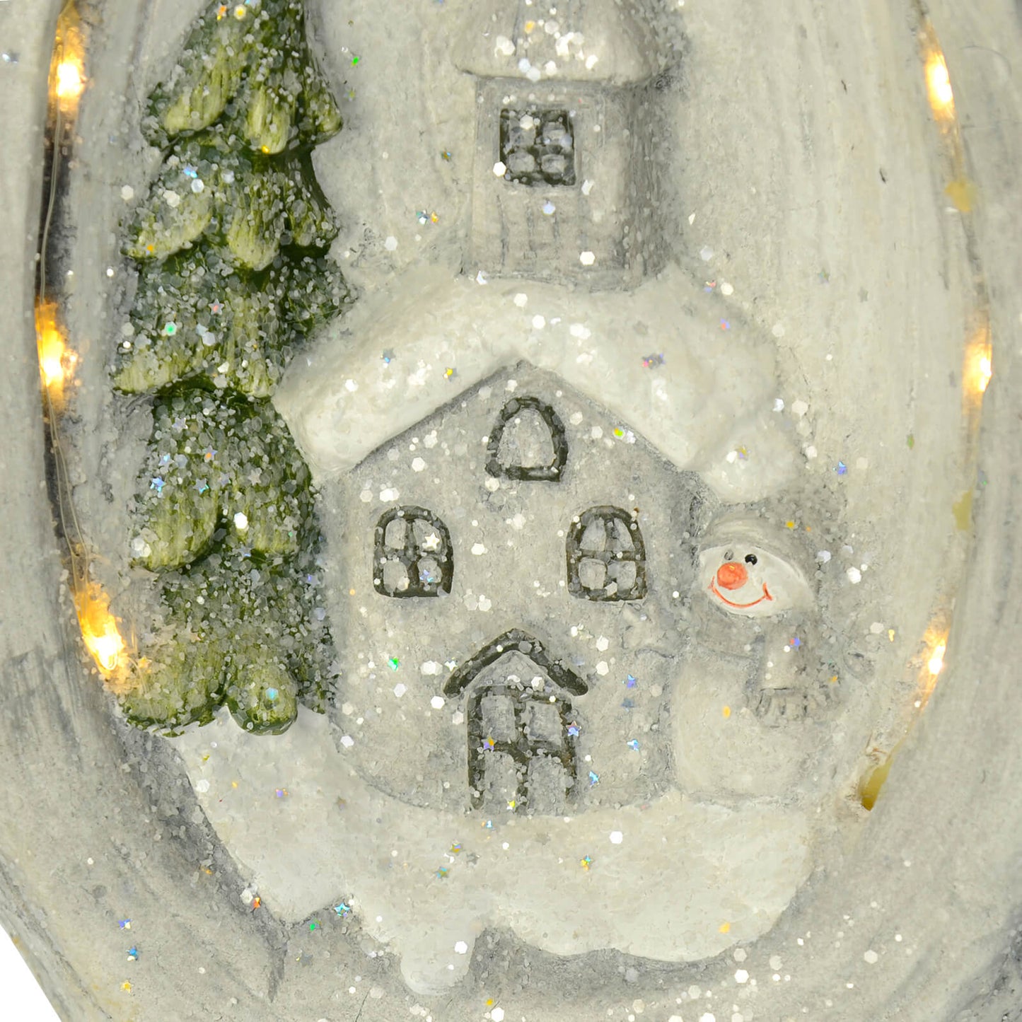 Close up detail of snowman, church and tree snow scene lit by warm white LED lights and sparkling iridescent glitter shapes