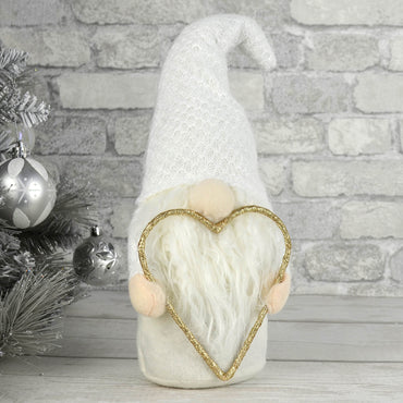 White fabric Christmas gonk decoration with glod glitter heart on a wooden table beside a silver Christmas tree tree