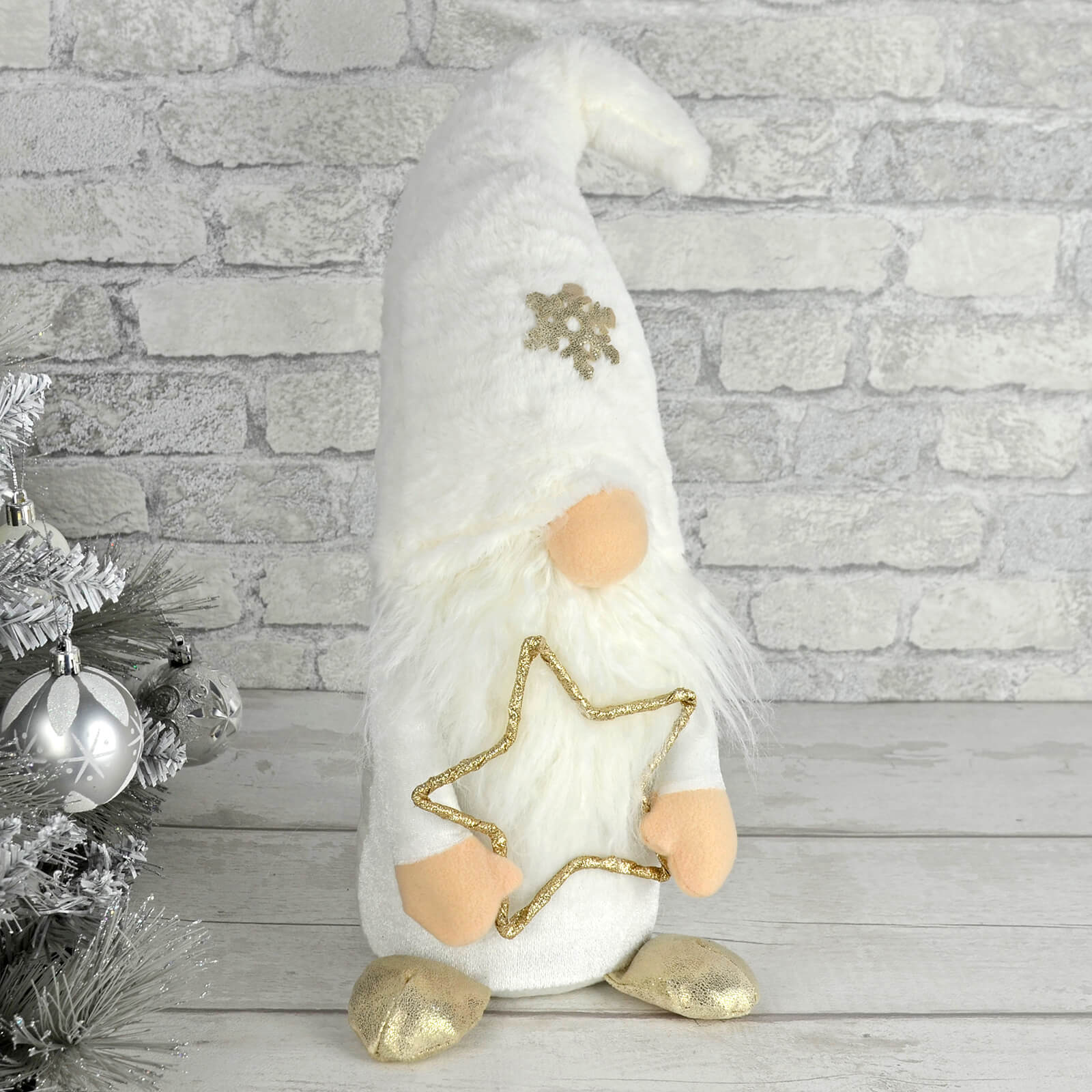 White fabric Christmas gonk figure decoration with gold glitter star standing on a wooden table beside a silver Christmas tree