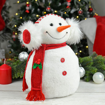 Snowman Christmas decoration figure with red scarf and fluffy earmuffs on a table with Christmas garland and candle