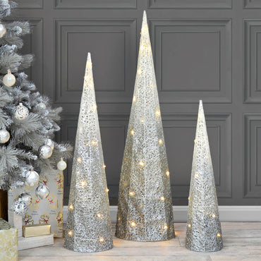 White to silver ombre tall cone shaped Christmas tree beside a silver decorated Christmas tree and presents 