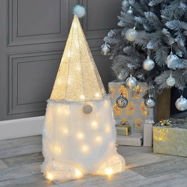 Light up Christmas gnome in silver and white with pom pom hat, sitting next to a decorated silver Christmas tree