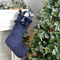 Navy blue faux fur Christmas stocking filled with presents hanging from a mantelpiece with lit up Christmas tree