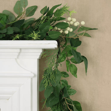 detail shot of mixed foliage natural berry christmas garland draped over fireplace mantel with sand colour wallpaper in the background