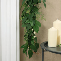 nature inspire christmas garland hanging over fireplace mantel, styled beside gre metal table featuring pillar candles