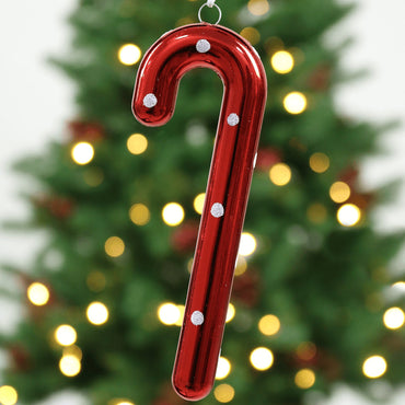 red glossy candy cane tree decoration hanging in front of christmas tree with warm white lights